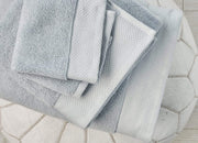 Light blue envello Bath Towels stacked on a white leather pouf